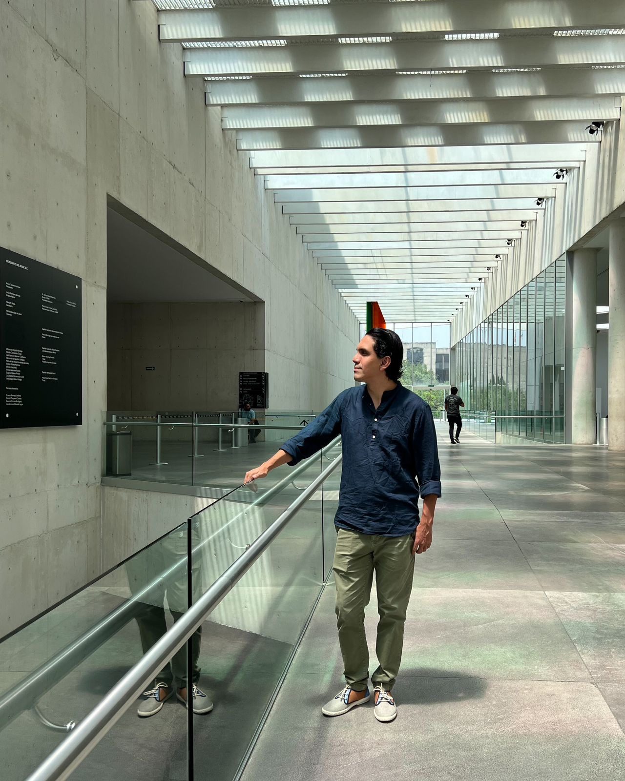 A man walking through a modern concrete and glass corridor of a city museum